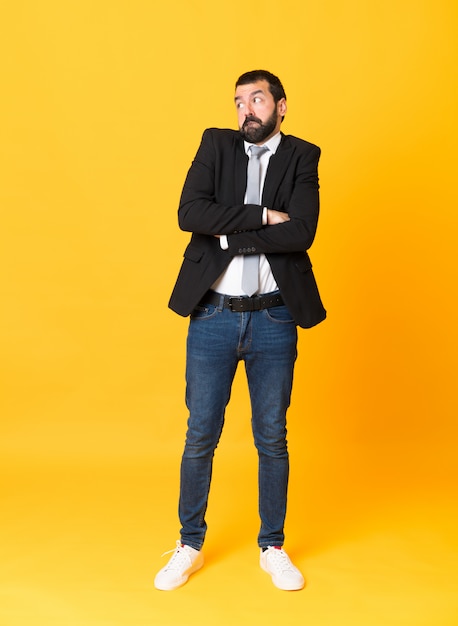 Full length  business man over isolated yellow wall making doubts gesture while lifting the shoulders