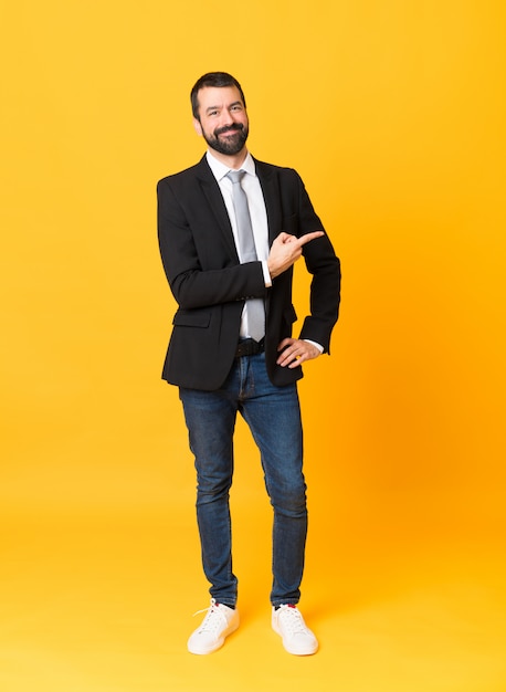 full length  of business man over isolated yellow wall pointing to the side to present a product