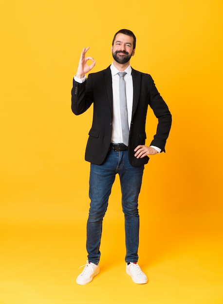 Full length  business man over isolated yellow wall showing ok sign with fingers