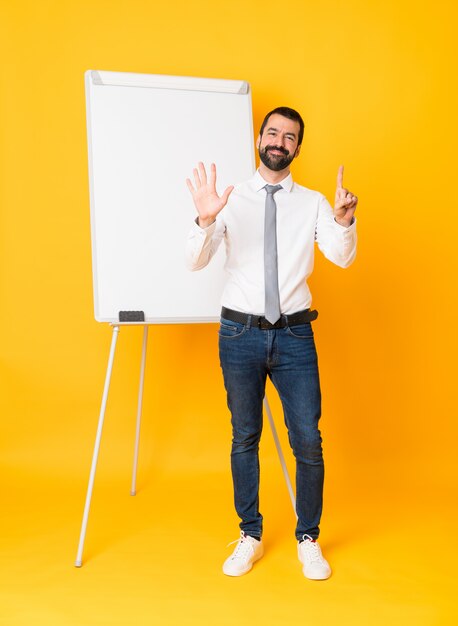 Full length  businessman giving a presentation on white board over isolated yellow wall counting six with fingers