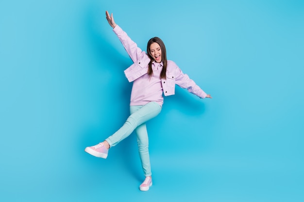 Full length of carefree teenage girl having fun dancing isolated on blue color background