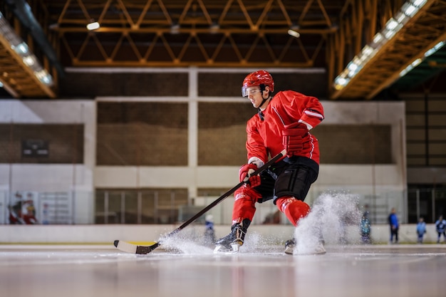 Full length of caucasian hockey player playing hockey on ice in hall.