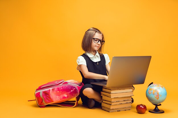 Full length caucasian schoolgirl sitting behind a stack of books working on laptop kids education