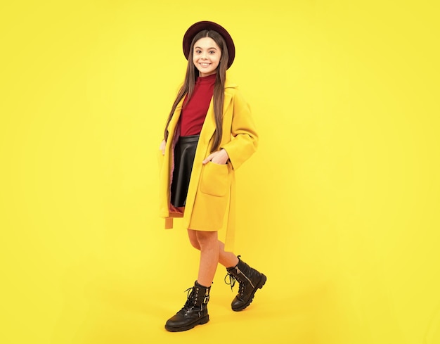 Full length of cheerful teenager child girl wearing comfy\
trendy fashion autumn coat isolated over yellow background happy\
teenager portrait mock up copy space