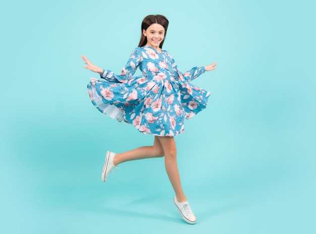 Full length cheerful teenager kid jump enjoy rejoice win isolated on blue background Small child girl in summer dress jumping Fashion trendy kids look child model in vogue fashionable style outfit
