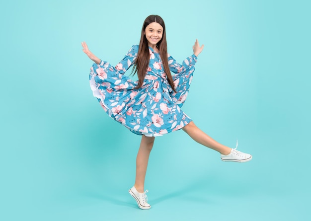 Full length cheerful teenager kid jump enjoy rejoice win isolated on blue background small child girl in summer dress jumping happy teenager positive and smiling emotions