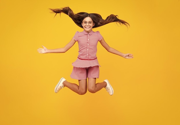 Full length cheerful teenager kid jump enjoy rejoice win\
isolated on yellow background small child girl in summer dress\
jumping amazed teen girl excited expression cheerful and glad