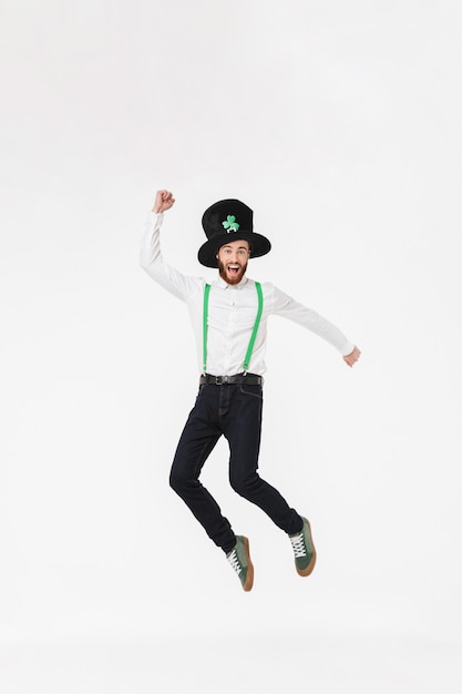 Full length of a cheerful young man celebrating StPatrick 's Day isolated over white wall, jumping