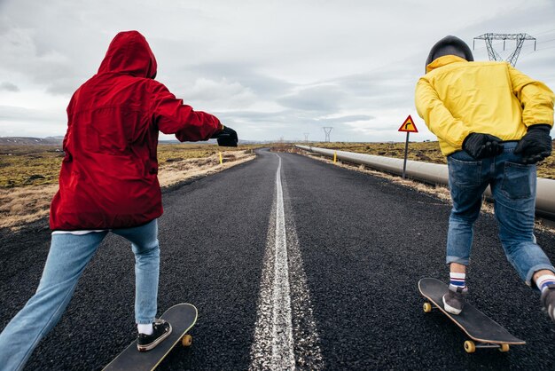 Foto lunghezza completa di coppia che fa skateboard sulla strada contro il cielo