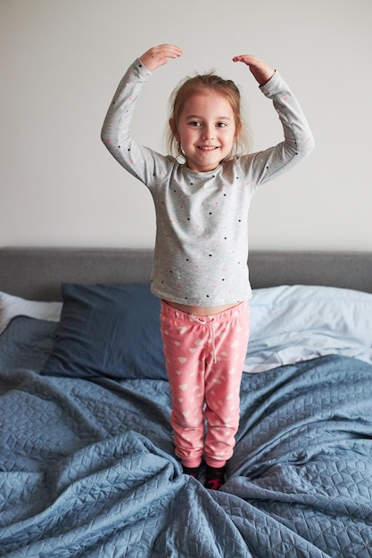 full length of cute girl standing on bed at home