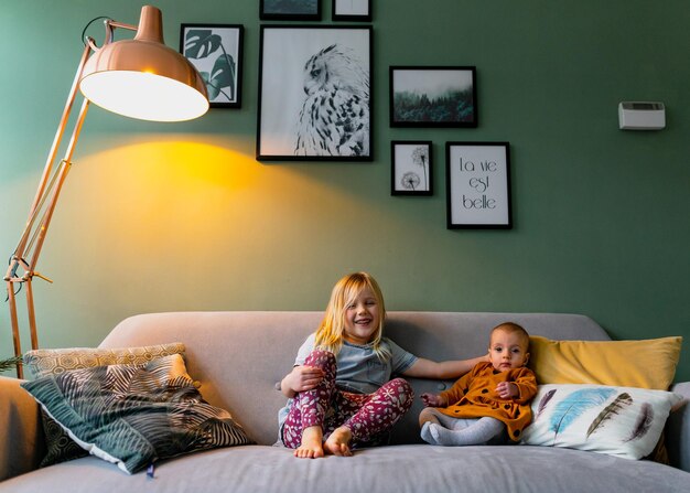 Full length of cute siblings sitting on sofa at home