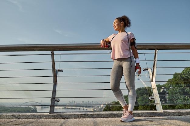 Per tutta la lunghezza di una deliziosa sportiva, atleta femminile con una corda per saltare, in piedi sul moderno ponte di vetro della città, rilassante dopo l'allenamento cardio all'aperto. sport, fitness, concetto di stile di vita attivo