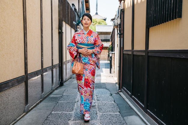 Photo full length of elegant female traveler with japanese traditional dress and walking in the alley in kyoto. asian young lady trying kimono robe in summer vacation. lady tourist travel in jp in holiday.