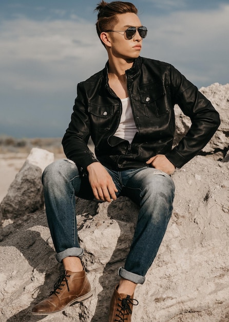 Foto lunghezza completa di un giovane alla moda che guarda lontano mentre è seduto su una roccia