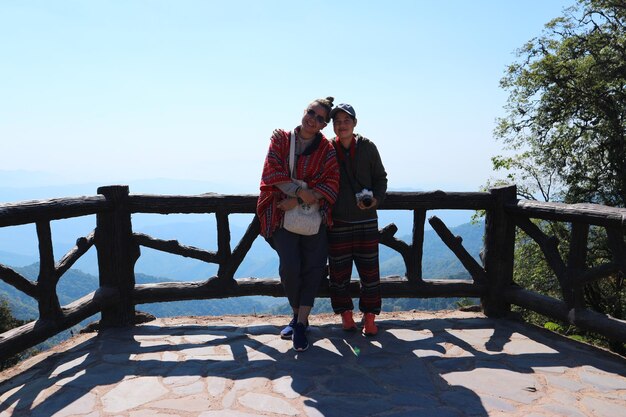 Photo full length of friends standing by railing on mountain against sky during sunny day