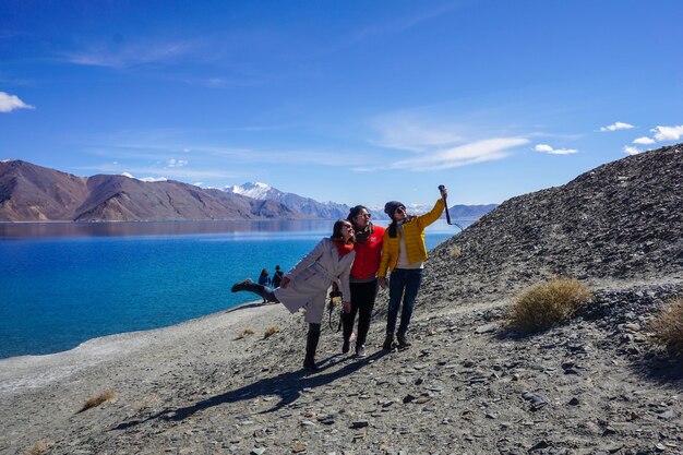 Photo full length of friends taking selfie while standing against lake