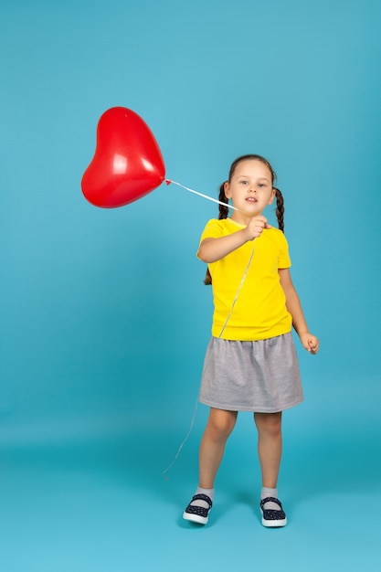 A full-length girl dances and waves a red balloon in the shape of a heart