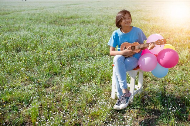 Full length of girl playing ukulele while holding balloons on plants