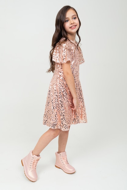 Full-length girl in shiny party dress posing on a white wall