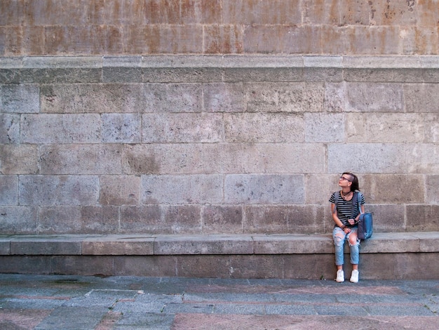 Photo full length of girl sitting against wall