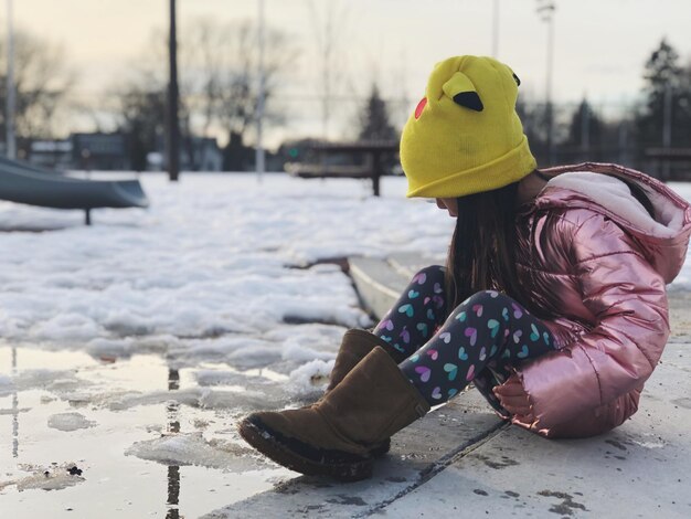 Foto lunghezza completa di una ragazza seduta sul sentiero durante l'inverno