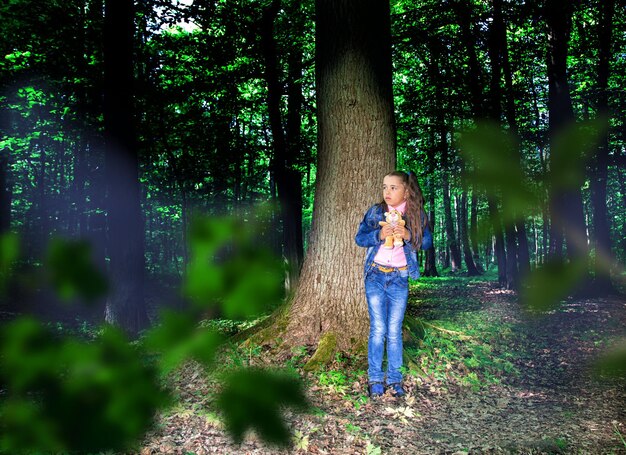 Foto lunghezza completa di una ragazza in piedi contro il tronco di un albero nella foresta