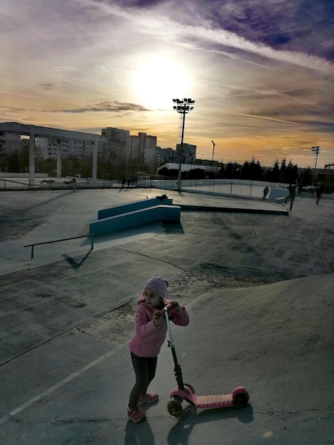 Photo full length of girl with push scooter against sky during sunset
