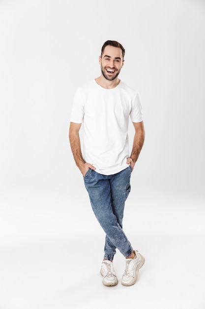 Full length of a handsome cheerful man wearing blank t-shirt standing isolated over white wall, posing