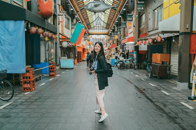 Per tutta la lunghezza del turista asiatico felice che si gira per guardare la fotocamera con un sorriso nel mezzo della sala giochi mentre visita il mercato di kuromon ichiba a osaka in giappone