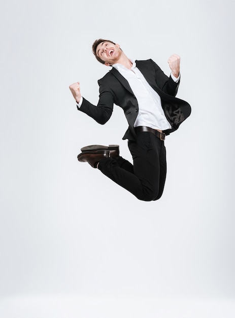 Full length happy business man in black suit jumping and celebrating success isolated on a white wall