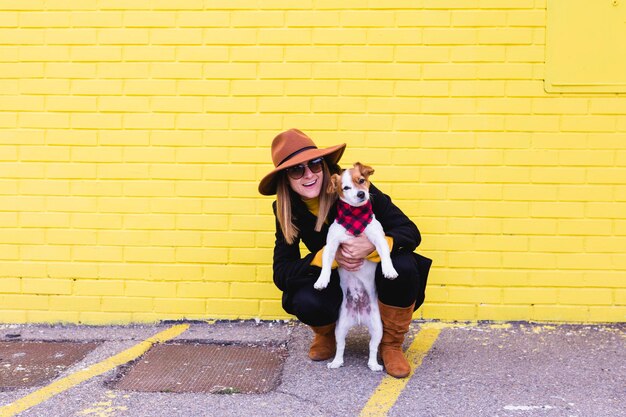 Foto lunghezza completa di donna felice che porta il cane contro la parete gialla