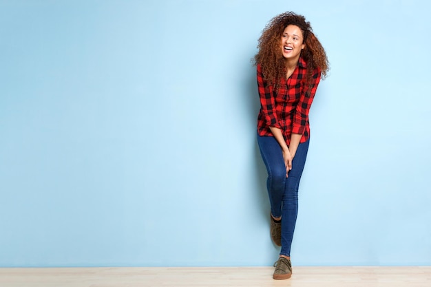 Full length happy woman leaning against blue background