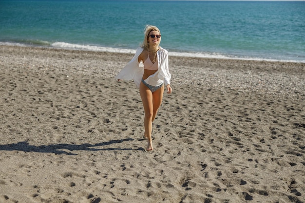 Tutta la lunghezza della donna felice in costume da bagno e occhiali che sembra eccitata mentre trascorre del tempo in riva al mare