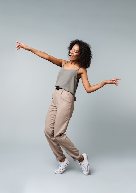 Full length of a happy young african woman casually dressed standing isolated, pointing at copy space