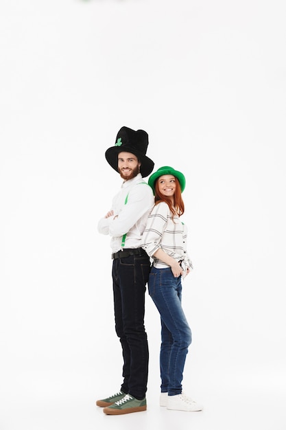 Full length of a happy young couple wearing costumes, celebrating StPatrick 's Day isolated over white wall