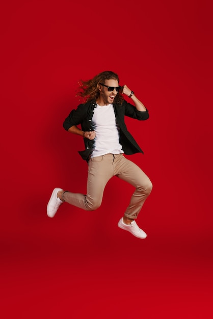 Full length of happy young man in casual clothing smiling and gesturing while hovering against red wall