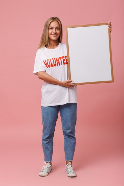 Full length of a happy young volunteer girl standing isolated, showing blank board