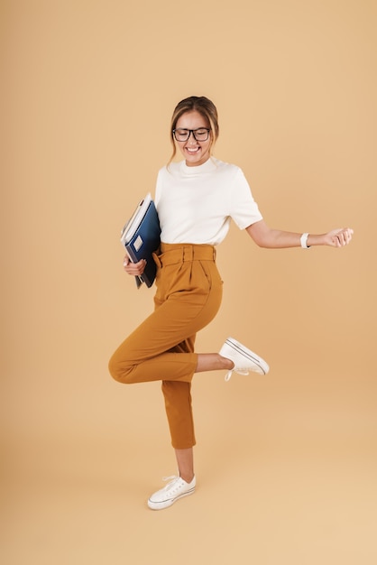 Full length image of brunette businesswoman wearing eyeglasses holding clipboard and register books isolated