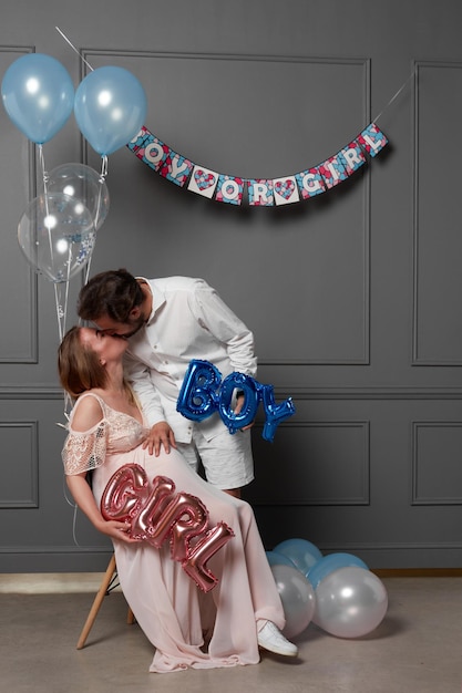 Photo full length image of a couple they kiss holding inscription boy or girl during gender reveals party grey background