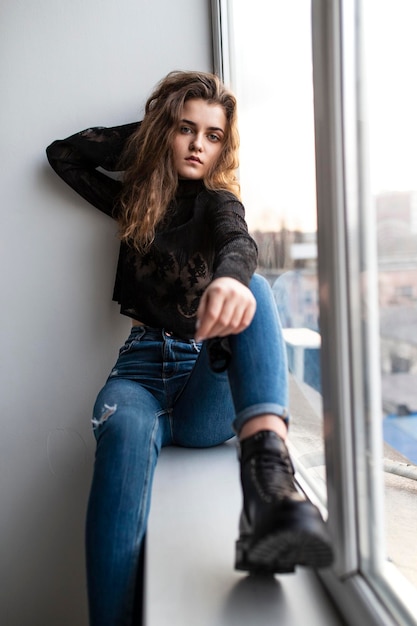 Full length image of a cute pensive gorgeous young woman with curly hair wear black blouse and jeans