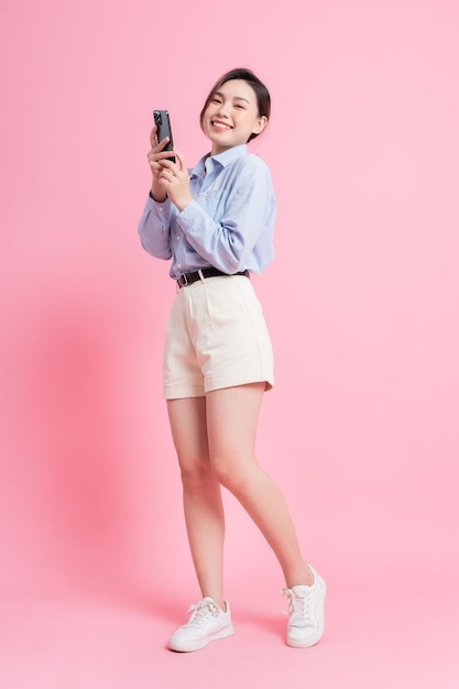 Full length image of young Asian girl using smartphone on pink background