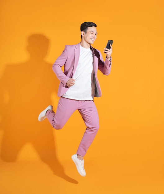 Full length image of young Asian man standing on orange background