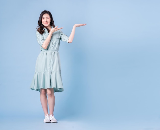 Full length image of young Asian woman wearing dress on blue background