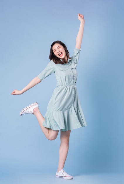 full length image of young asian woman wearing dress on blue background
