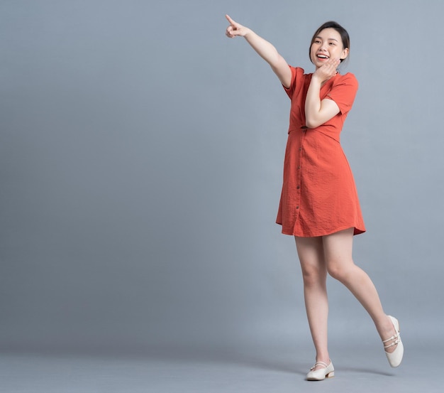 full length image of young asian woman wearing orange dress on gray background
