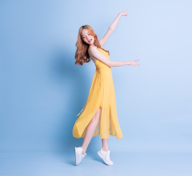 Full length image of young Asian woman wearing yellow dress on blue background