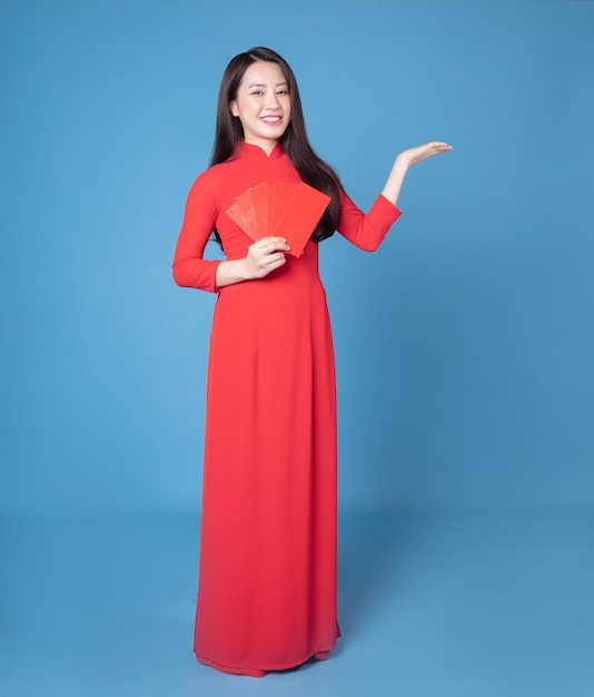 Full length image of young Vietnamese woman wearing red ao dai on background