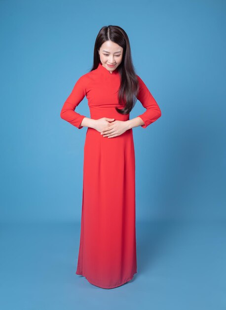 Full length image of young Vietnamese woman wearing red ao dai on background