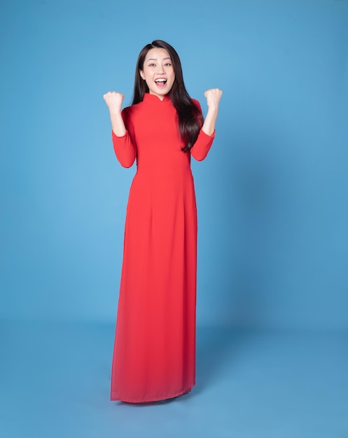 Full length image of young Vietnamese woman wearing red ao dai on background