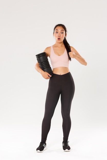 Full length of impressed and satisfied asian female athlete, fitness girl in activewear showing thumbs-up and say wow, tried new foam roller after workout to reduce soreness 